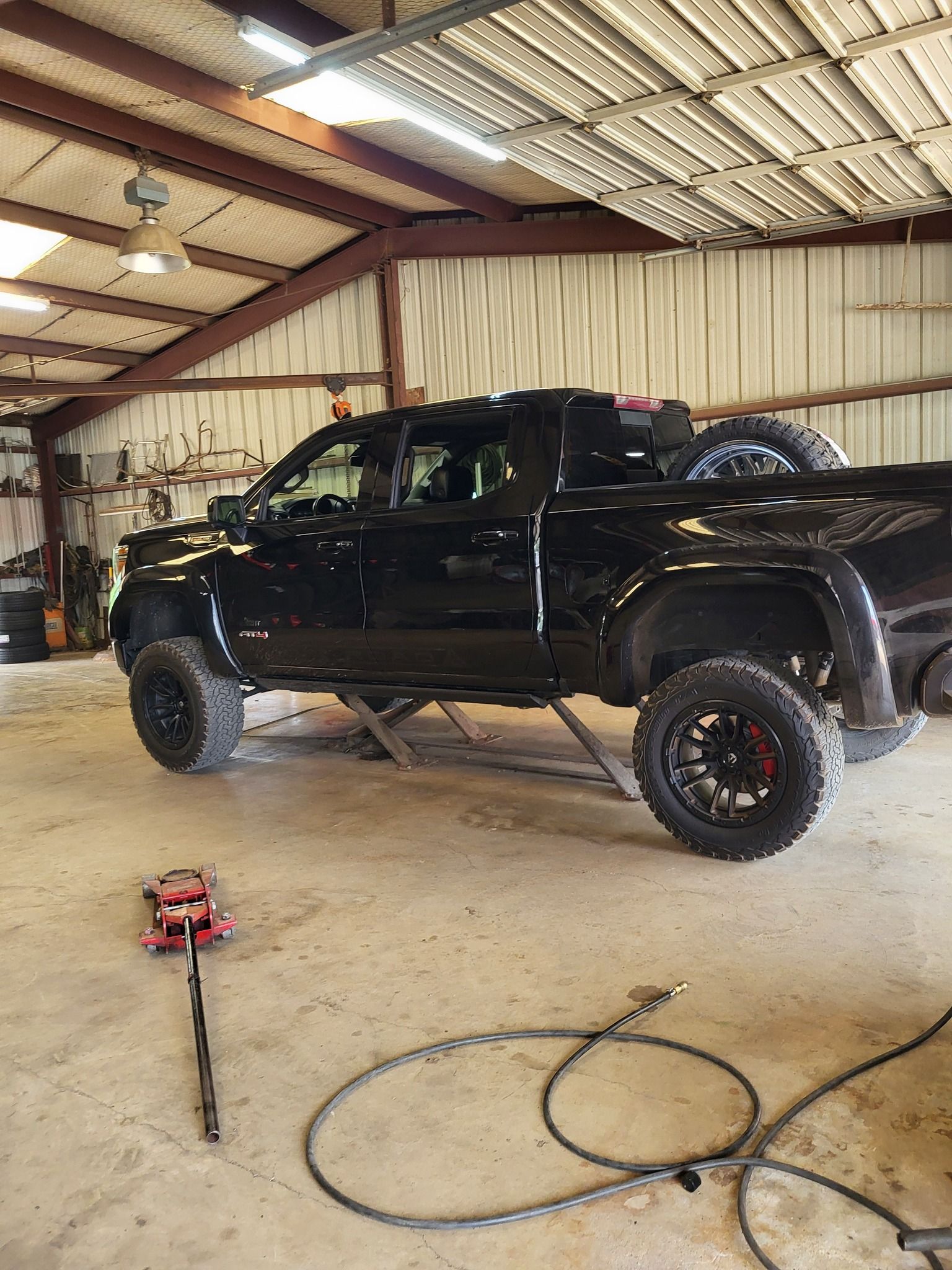 Black lifted pickup truck in a garage, with tools and hoses on the floor.