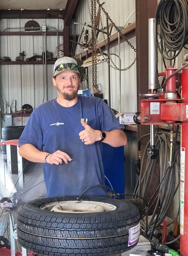 Mechanic in blue shirt giving thumbs-up behind a tire in a workshop