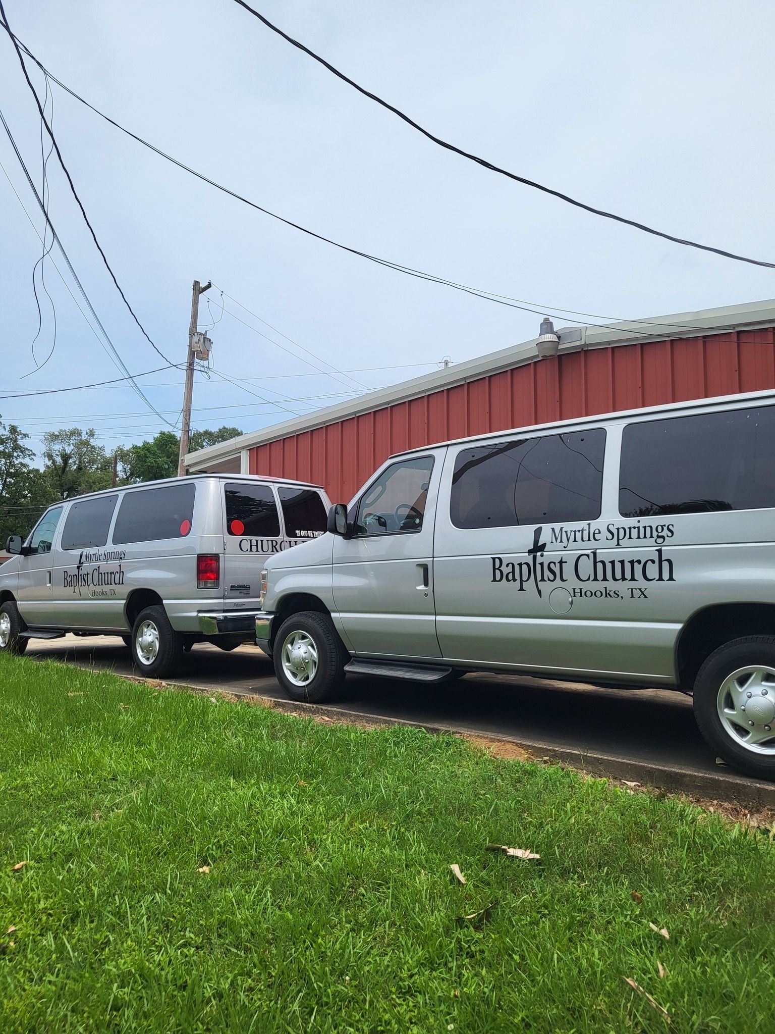 Two white vans parked by a red building on a grassy roadside, one labeled “Park’s Church”