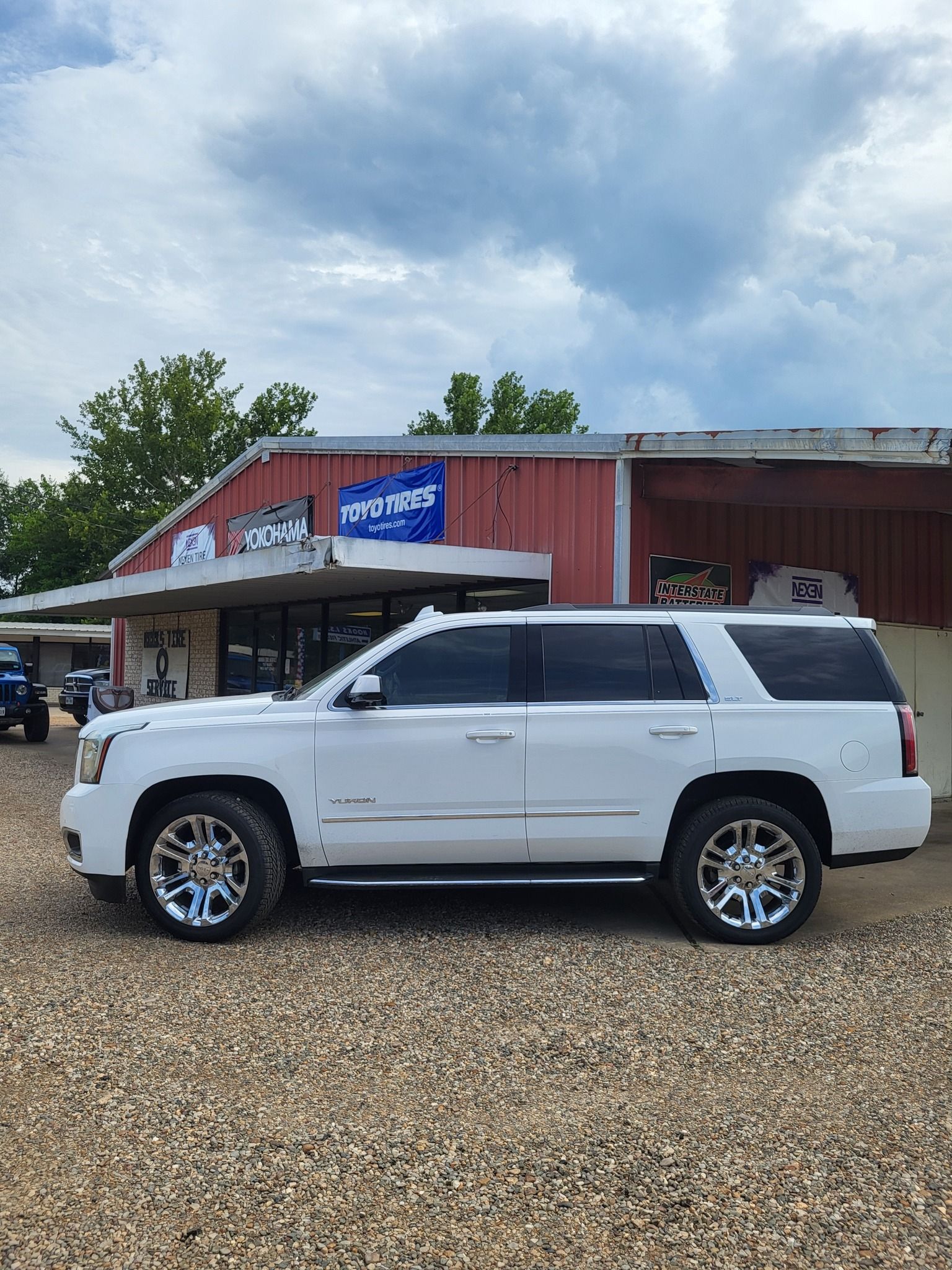 White SUV parked in front of a red building with a blue sign on a gravel lot