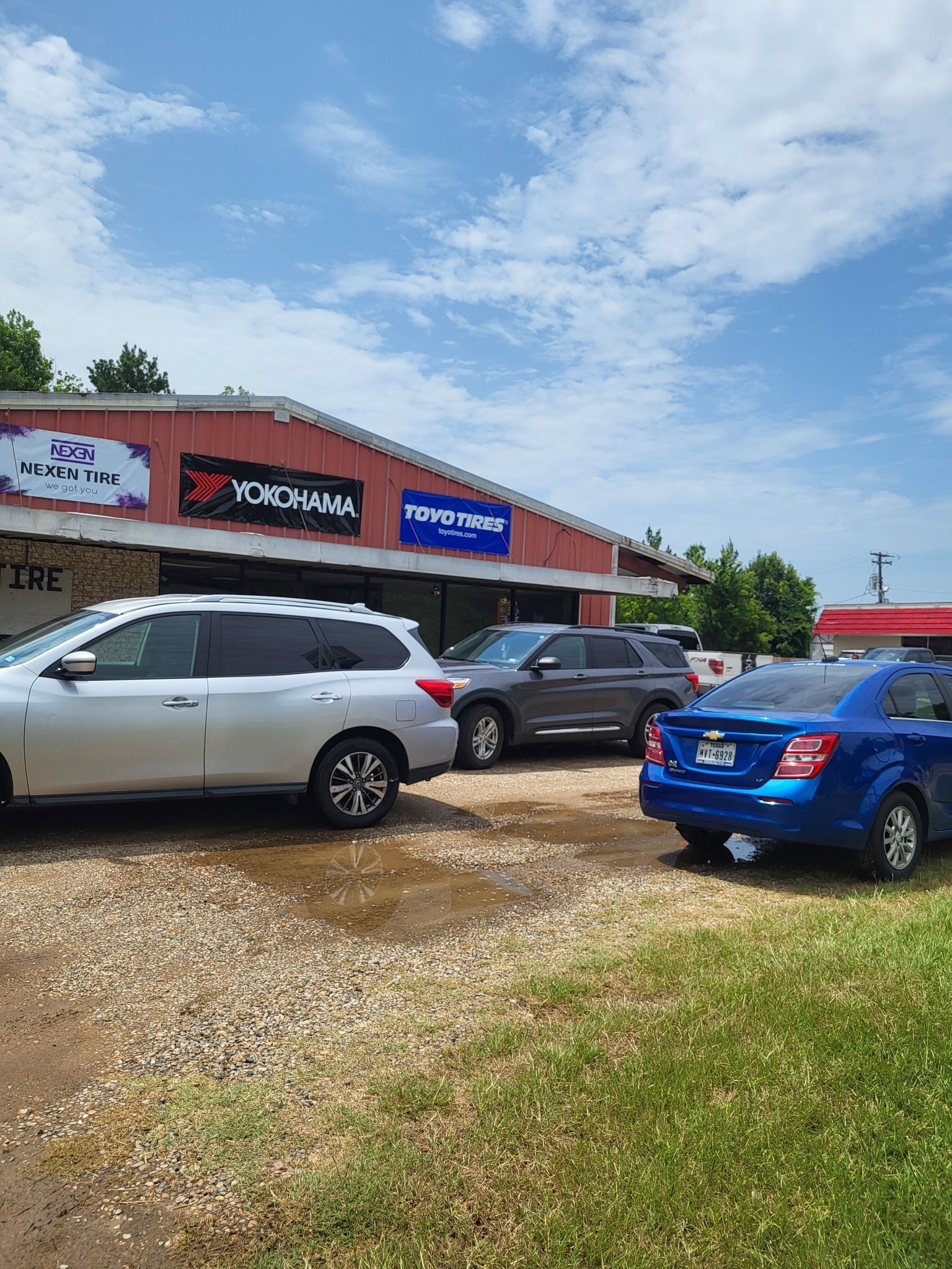 Parked cars outside a low brick storefront under a blue sky with signs on the building