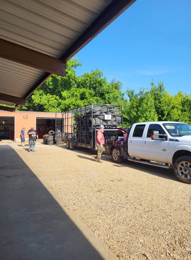 White pickup truck parked beside a stacked cargo trailer under a metal canopy on a gravel lot.