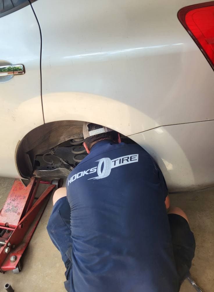 Mechanic working under the rear wheel well of a white car on a red jack in a garage