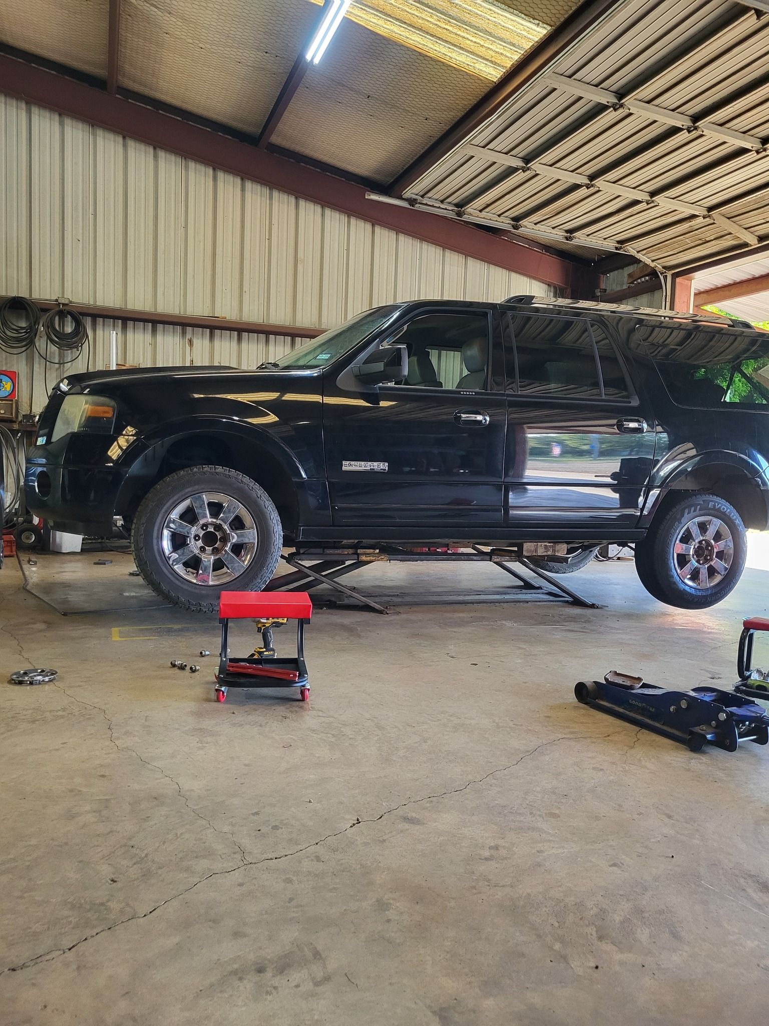 Black pickup truck lifted on jacks in a garage workshop, with tools on the floor.