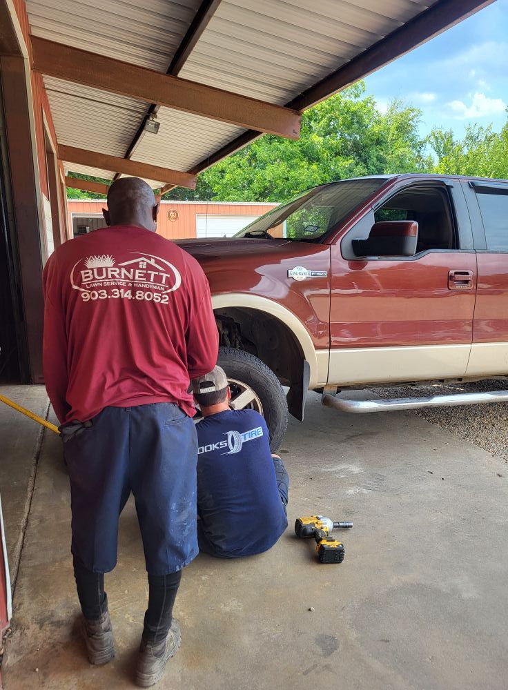 Mechanic working beside a red pickup truck under a carport, with tools on the ground.