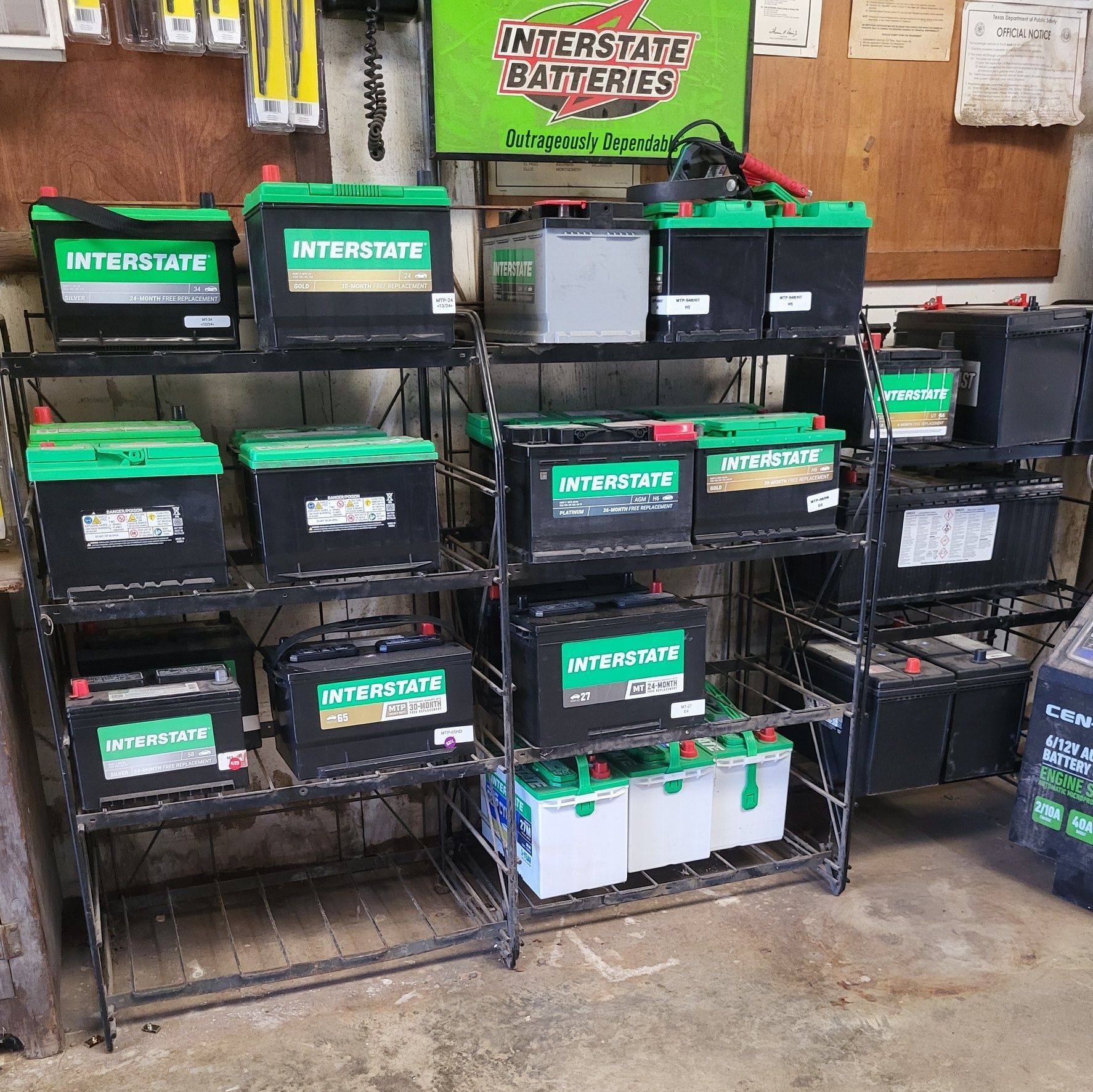 Shelves of Interstate car batteries with green labels in a garage or shop setting