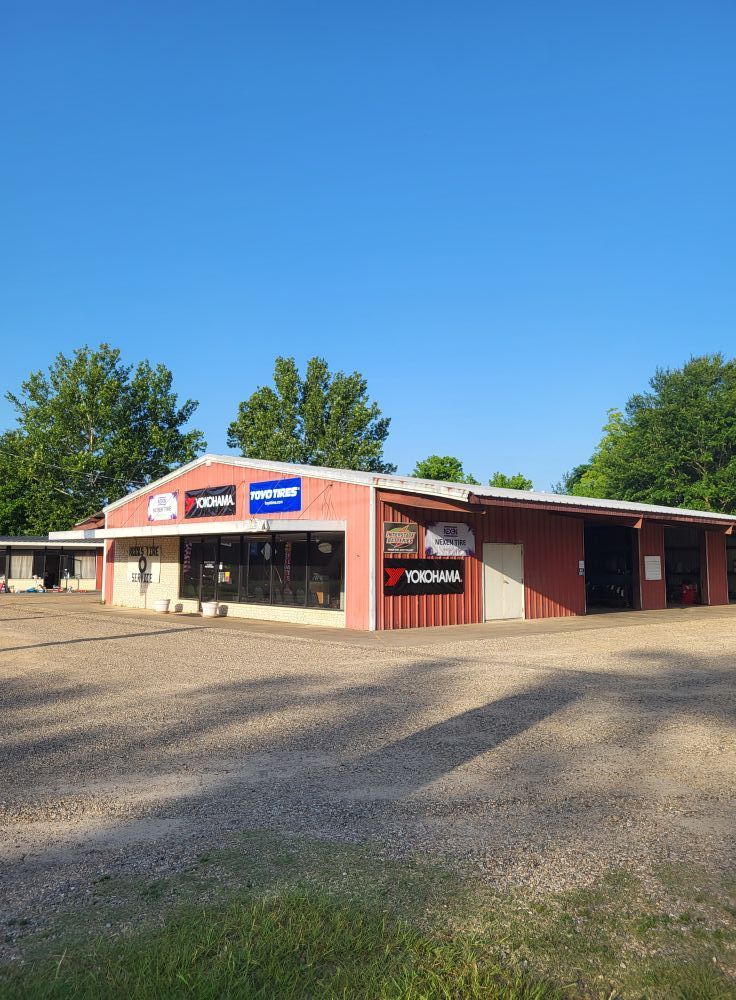 Small red-and-beige roadside building with storefront signs under a clear blue sky, surrounded by trees.