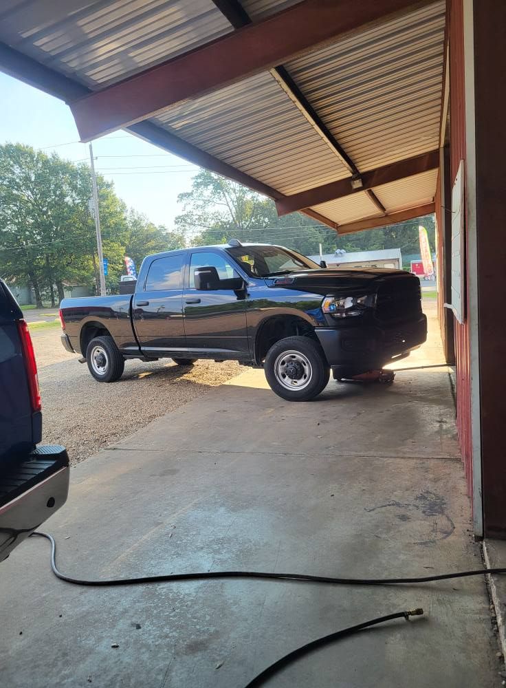 Black pickup truck parked under a metal carport next to a concrete driveway