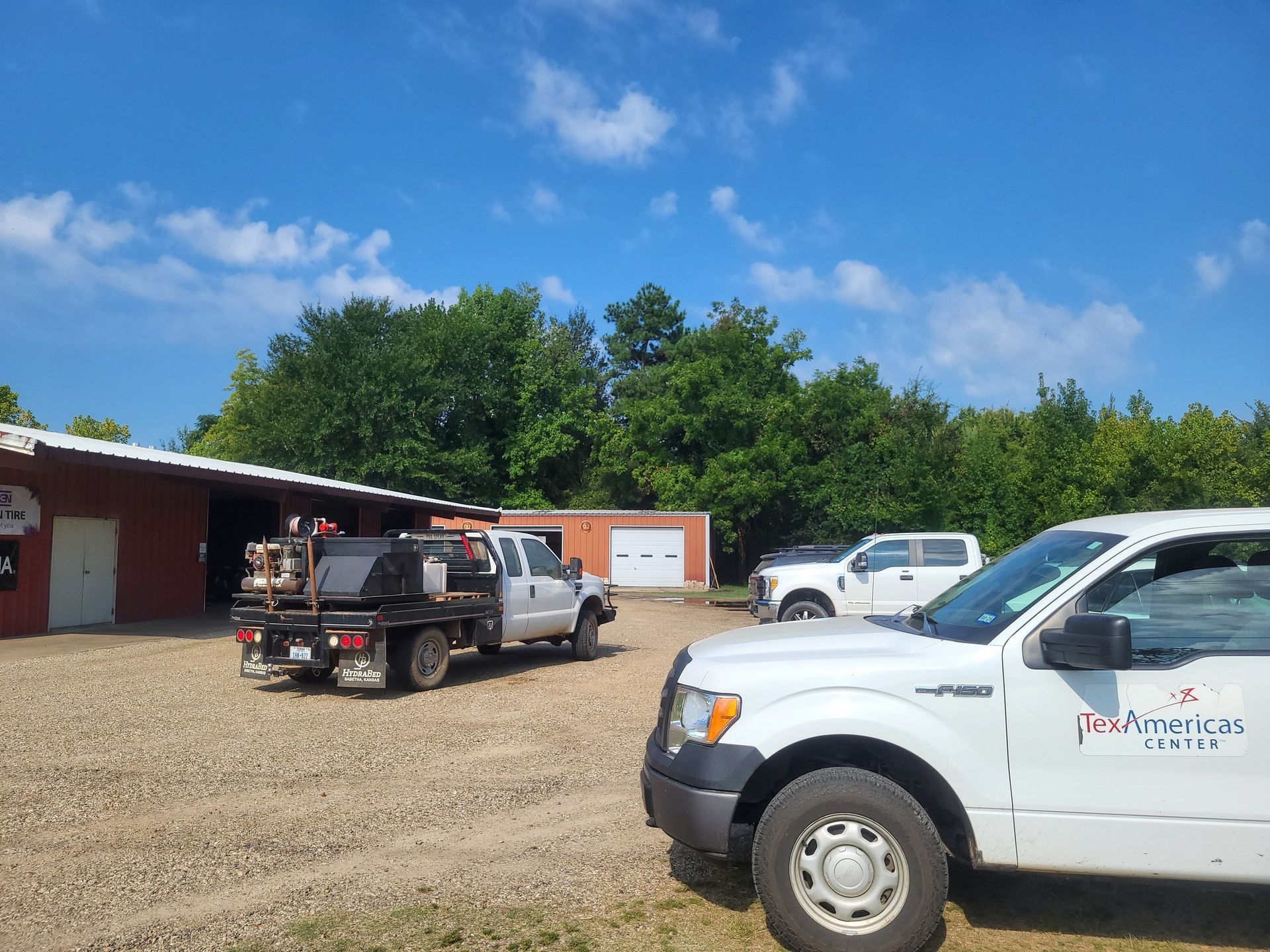 Pickup trucks parked on a gravel lot by a red building under a blue sky