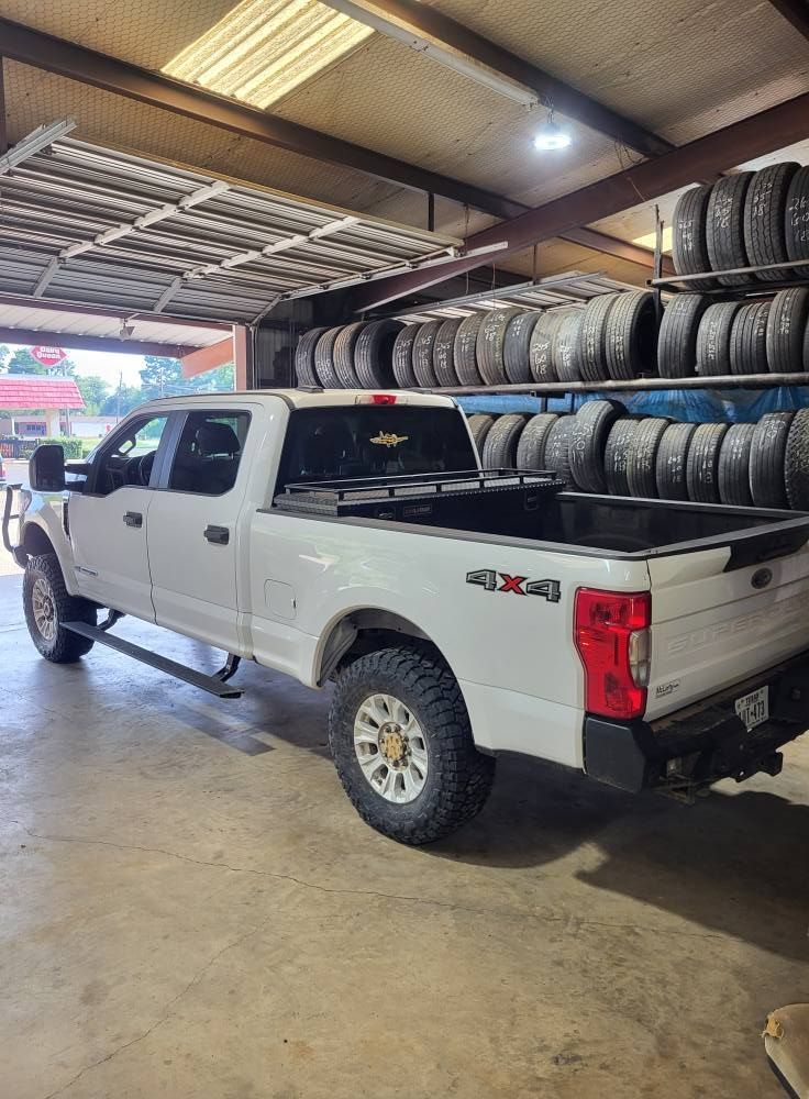 White Ford pickup truck inside a tire shop, parked beside stacks of tires on racks