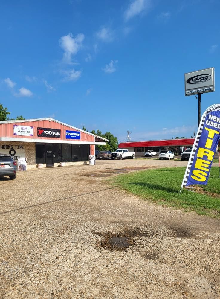 Car dealership lot with red-roofed building, parked cars, and a blue tire sign under a clear sky.