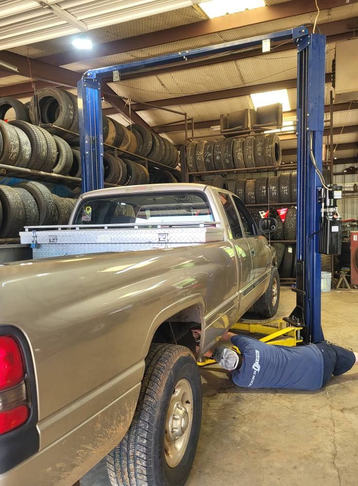 Lifted pickup truck in an auto shop with mechanic working underneath near stacked tires