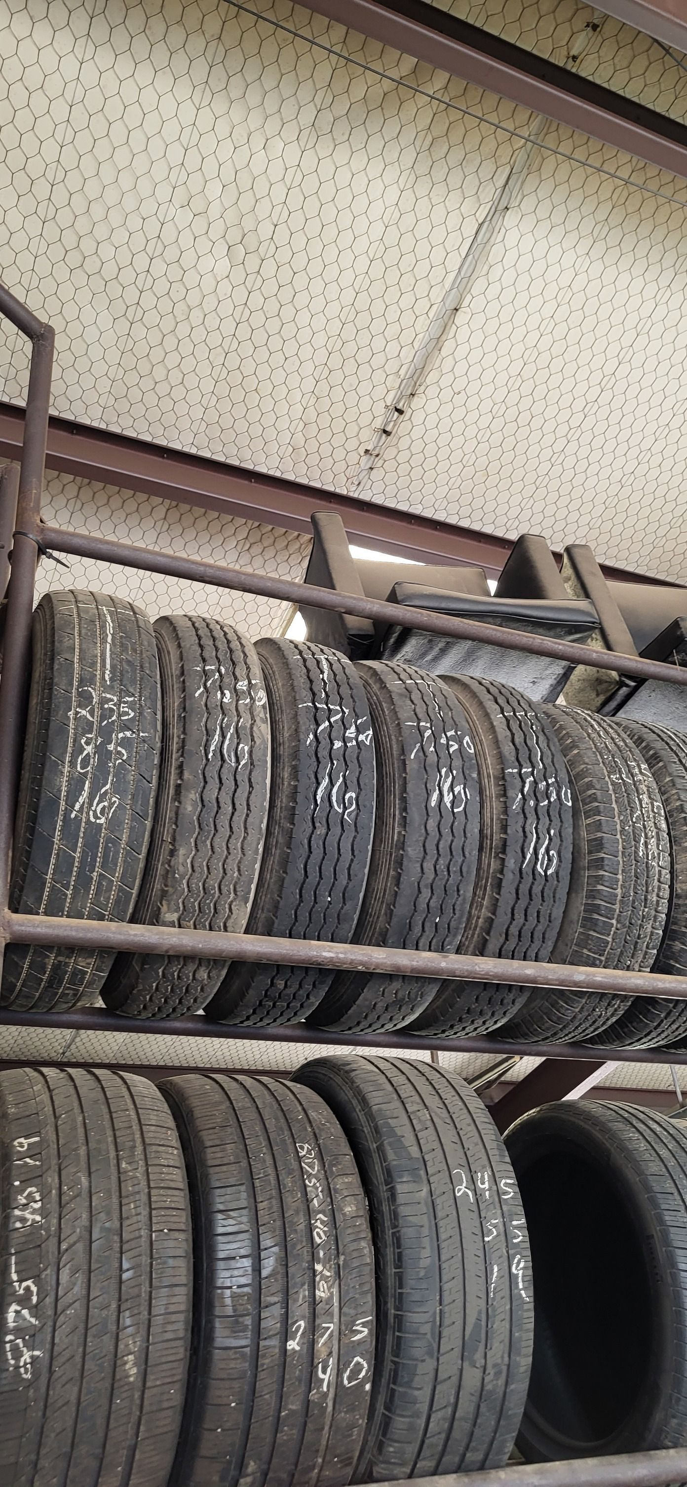 Stacked tires on metal shelves in a warehouse, with a perforated ceiling above.