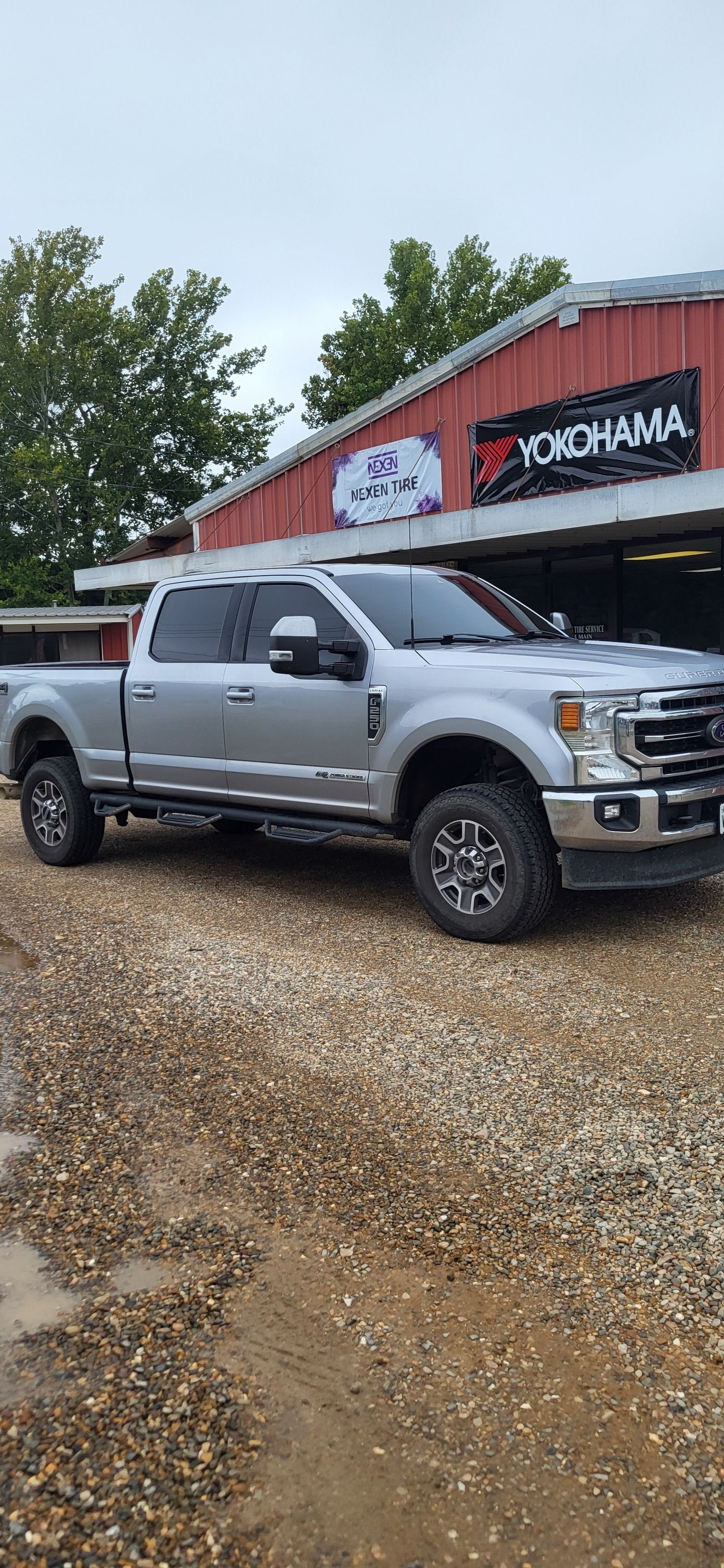 Silver pickup truck parked on gravel in front of a red building with signage.