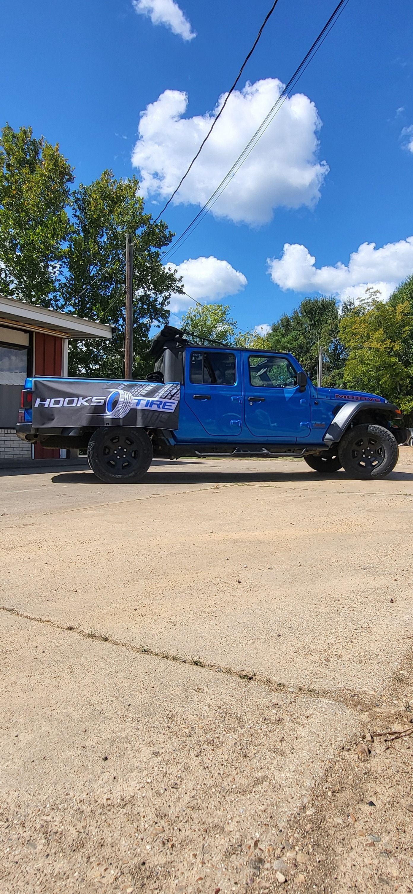 Blue flatbed tow truck parked on a sunny gravel lot under a blue sky