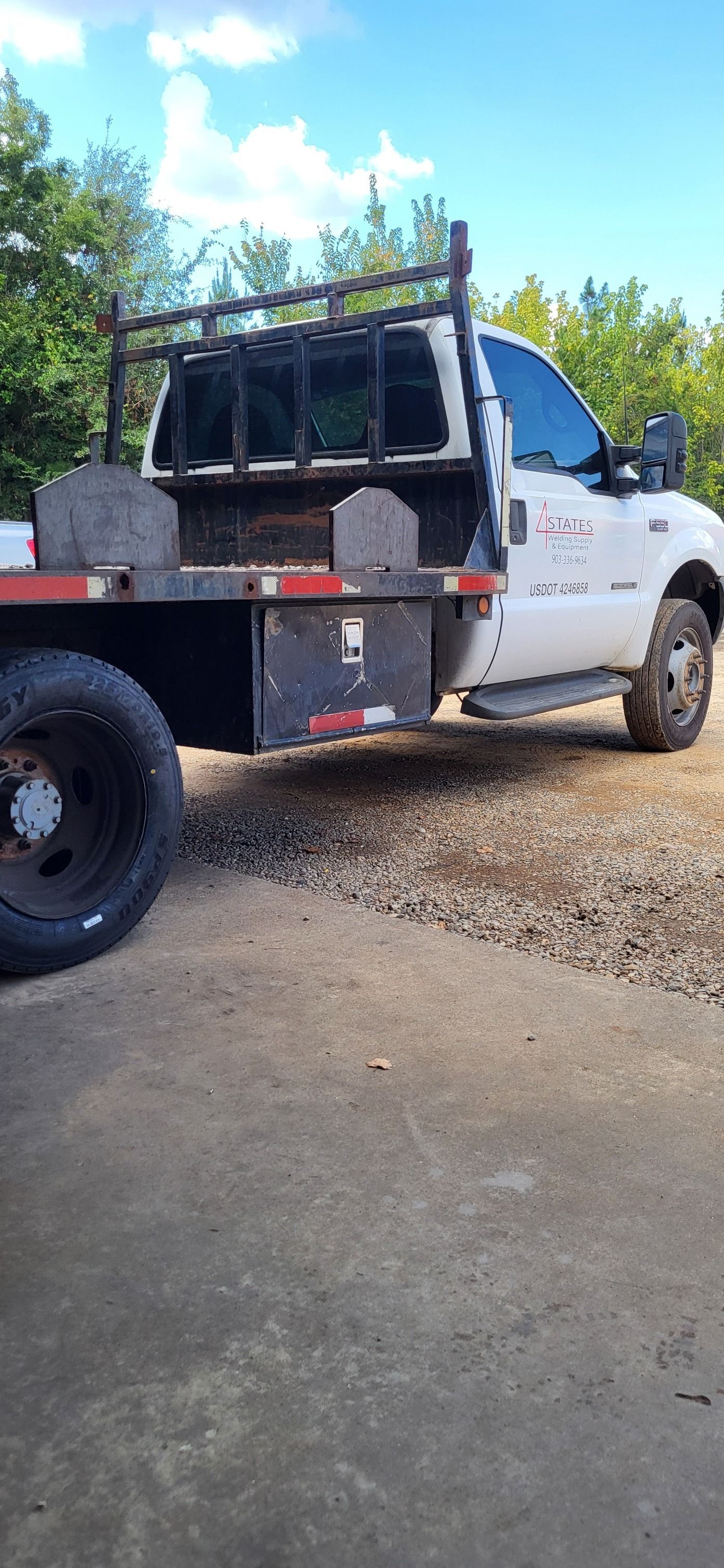 White utility truck with a flatbed parked on a gravel driveway beside a concrete path and trees