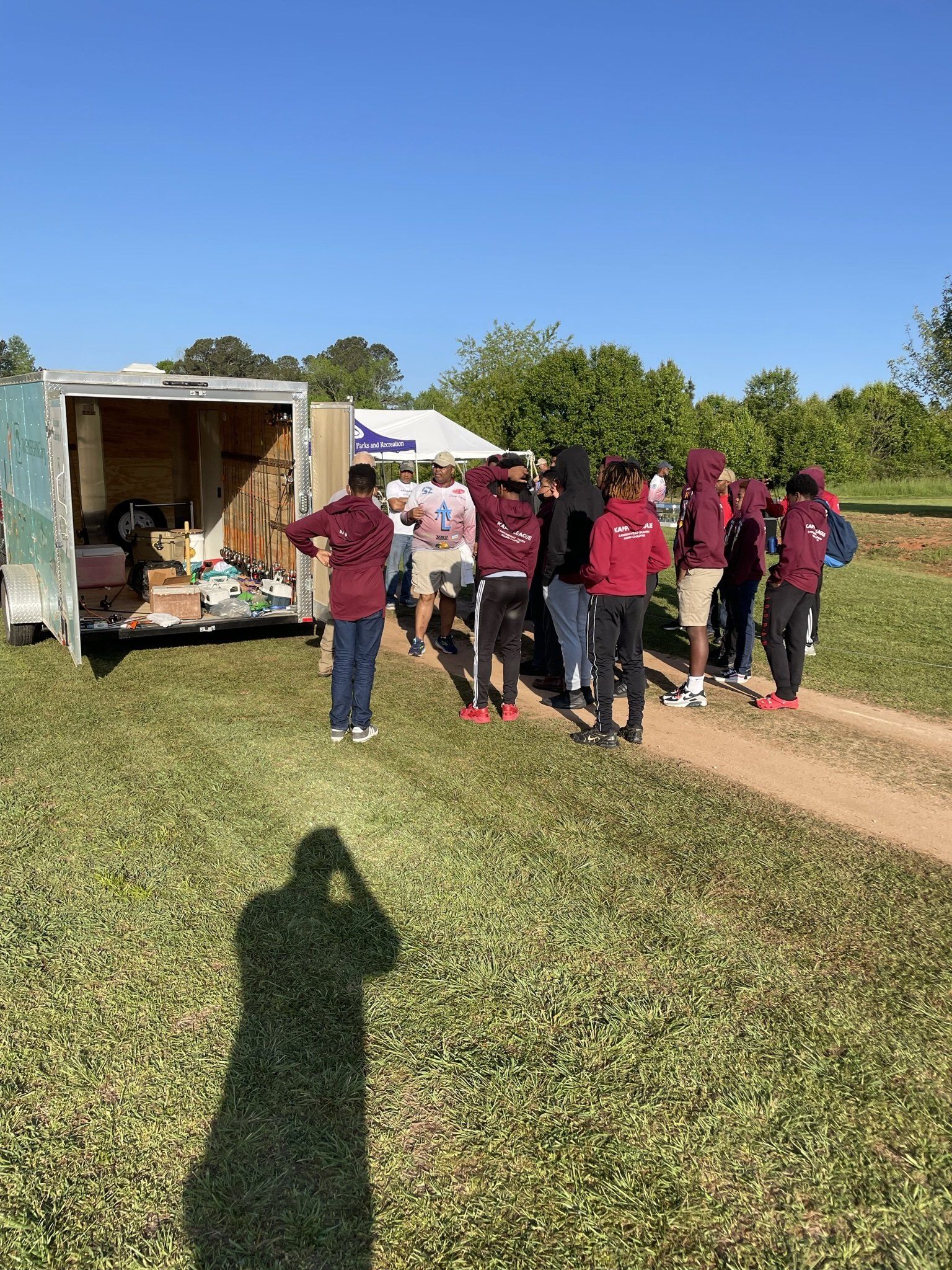 Group of people standing near a trailer on a grassy field under a clear blue sky.