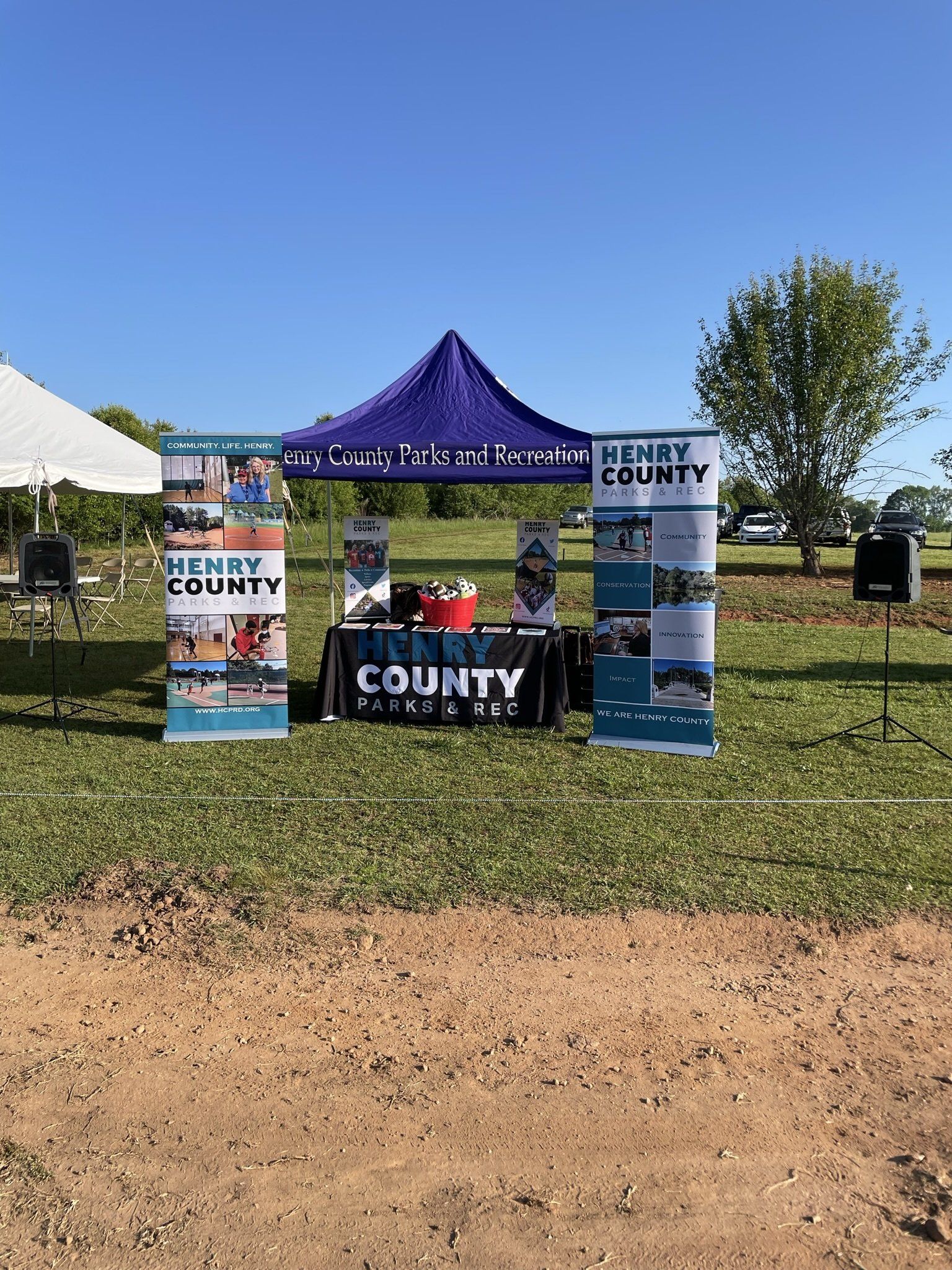 Henry County, GA, information booth. A tent with banners, table, and giveaways set up on grass under a clear blue sky.