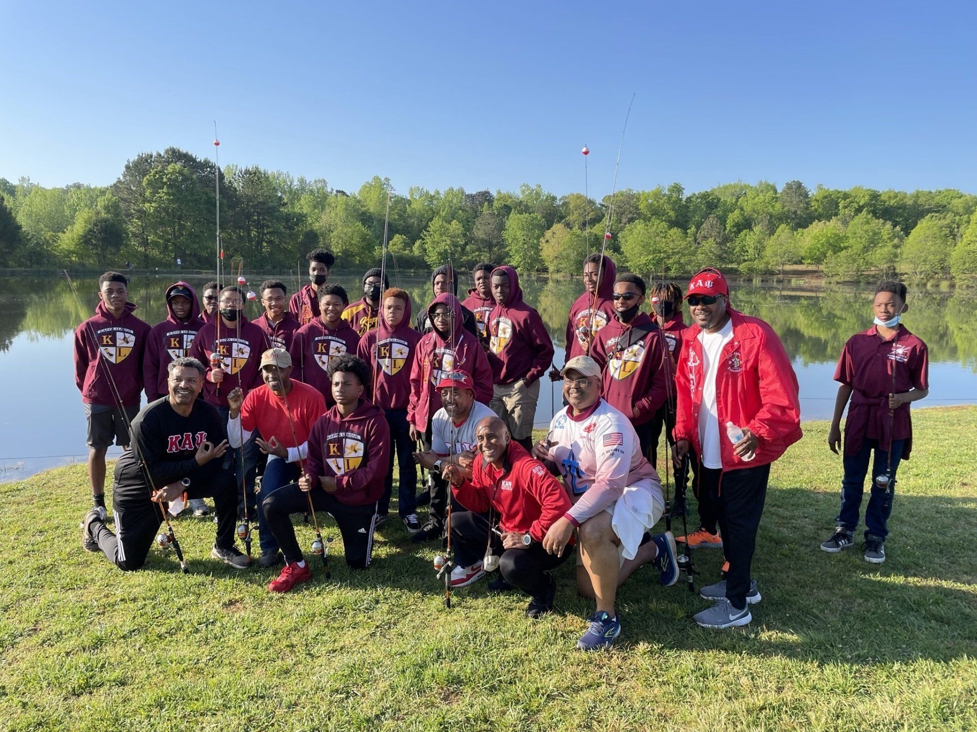Group of people in maroon and red clothing pose by a lake for a photo.
