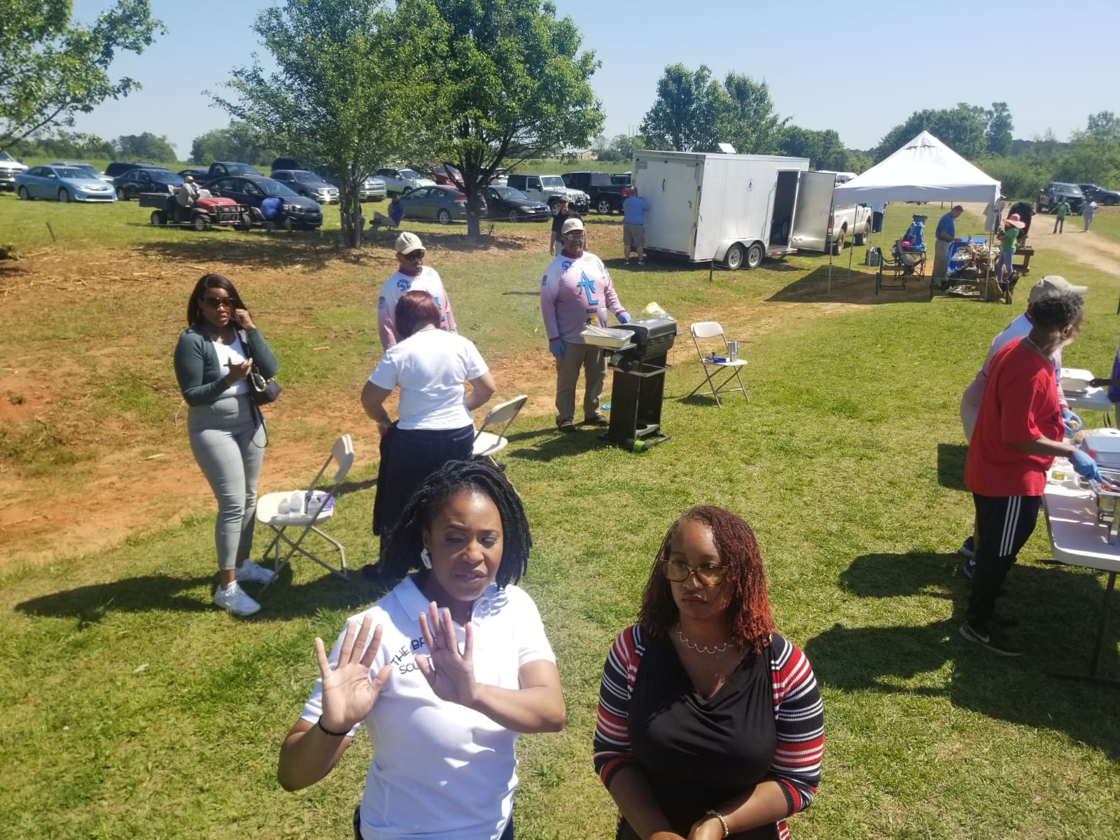 People at a picnic in a sunny field; grilling food, socializing, and setting up tables.