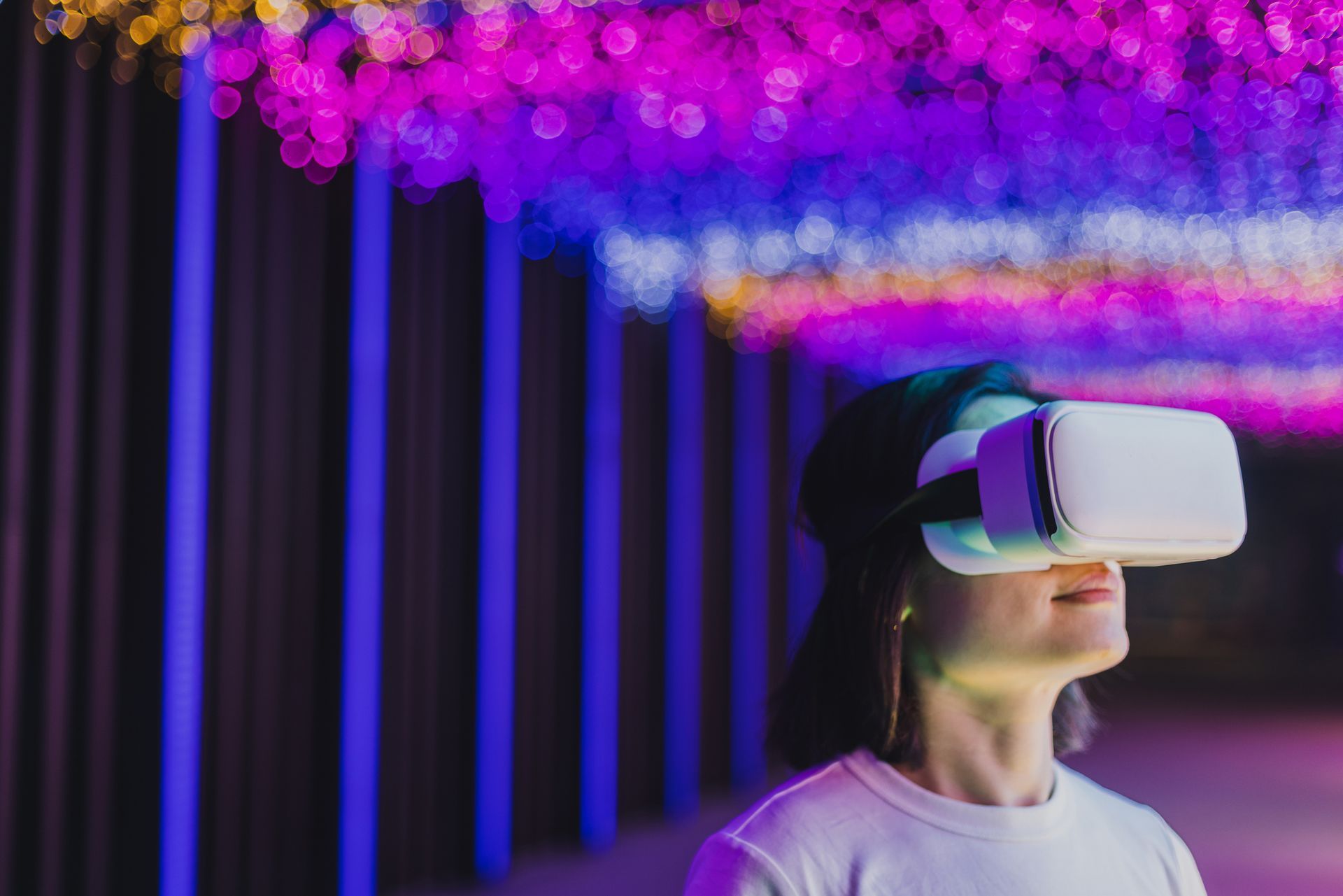 Donna che indossa un visore VR e osserva le luci al neon colorate in un ambiente buio.