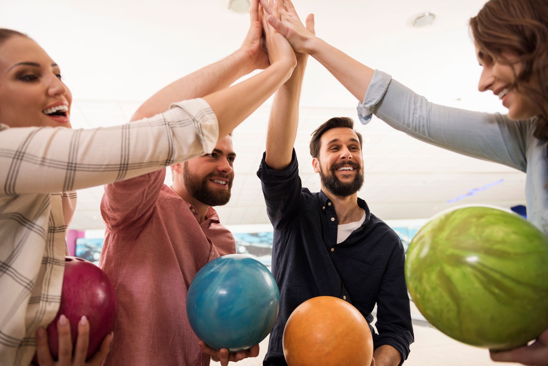 Amici che si danno il cinque al bowling. Tengono in mano le palle da bowling e sorridono.