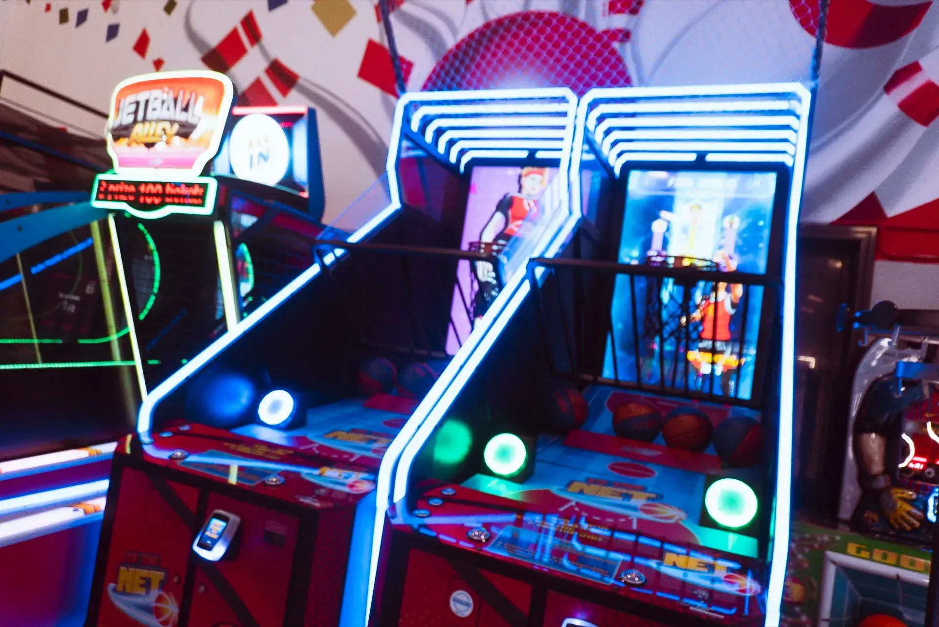 Due videogiochi arcade da basket, rossi con luci blu e bianche, con palloni da basket sul pavimento.