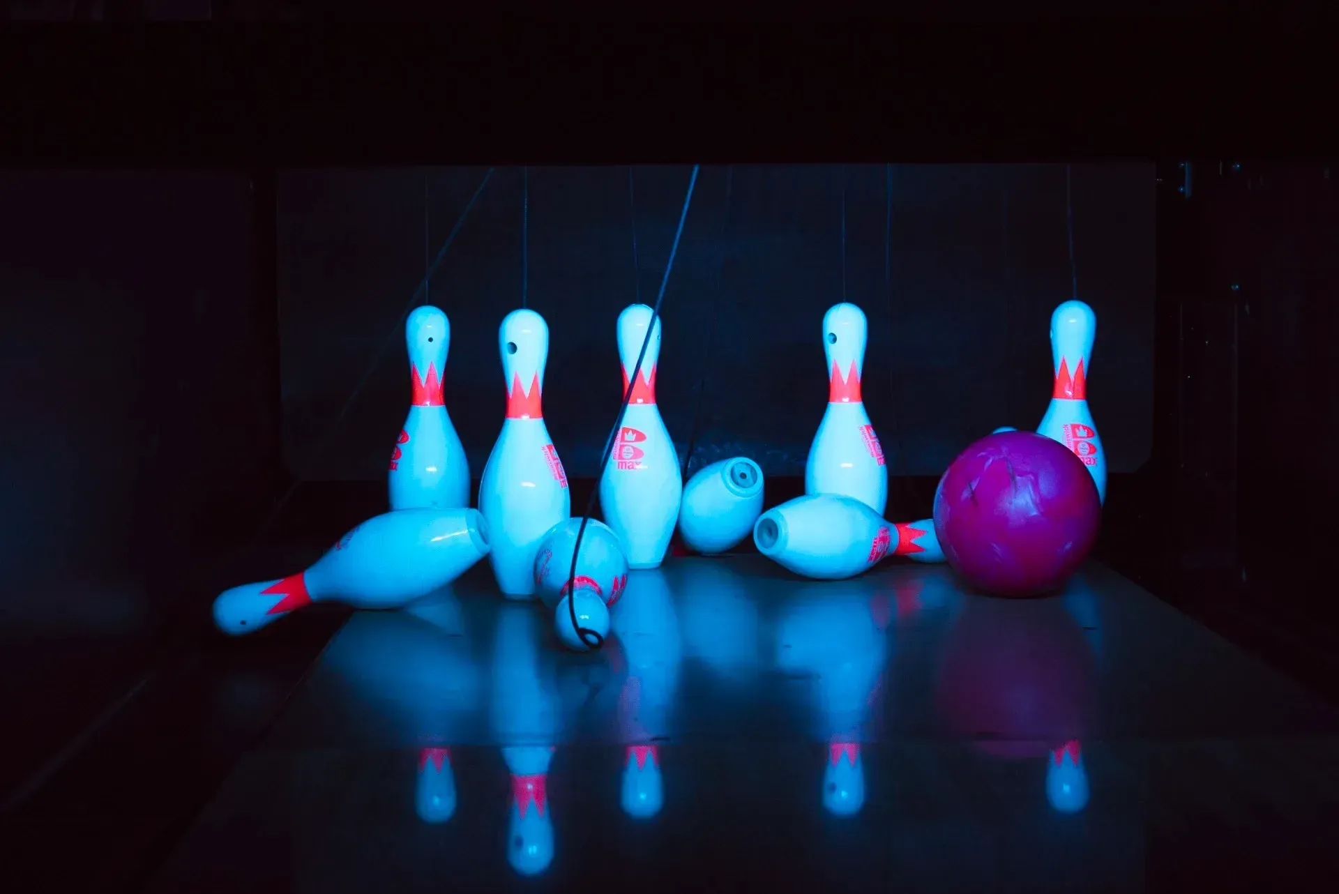 Birilli e palle da bowling su una pista, illuminati di blu e rosa, dopo essere stati colpiti.