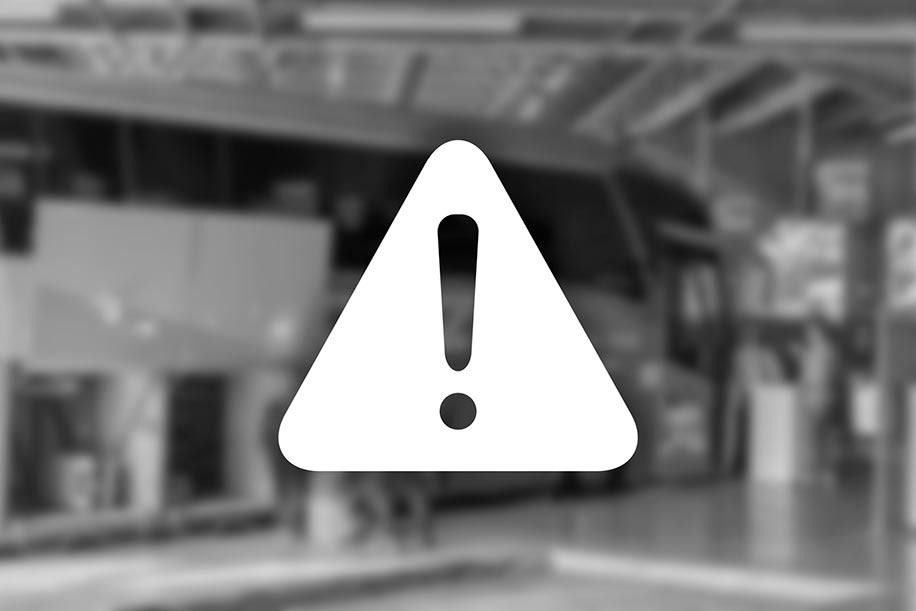 Ponto de exclamação branco dentro de um triângulo sobreposto a uma cena desfocada de uma estação de ônibus.