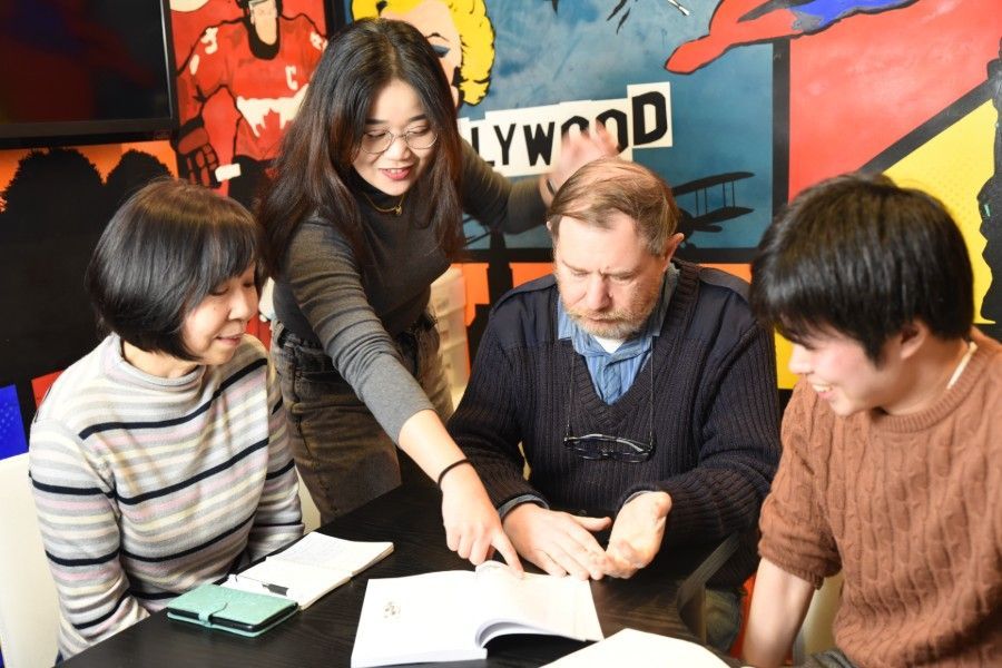 Four people gathered around a table, pointing at an open book in a colorful room.