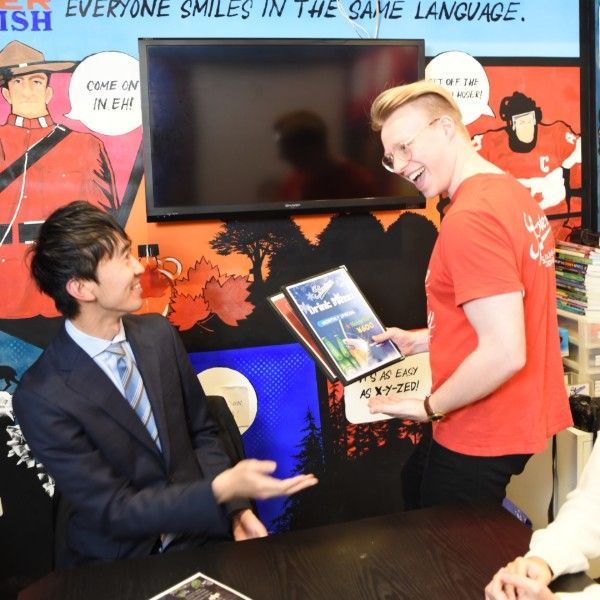 Two men are talking in front of a sign that says everyone smiles in the same language