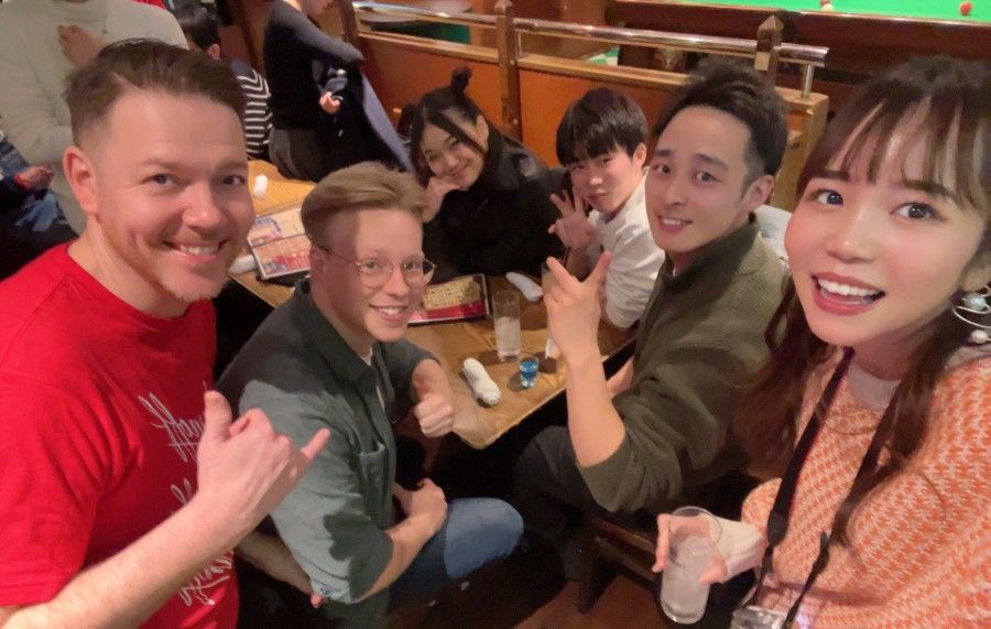 Four friends smiling and posing at a restaurant table, holding up shaka signs.