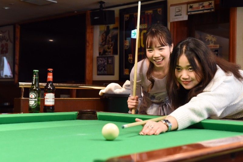 二人の女性がバーで一緒にビリヤードをしています。