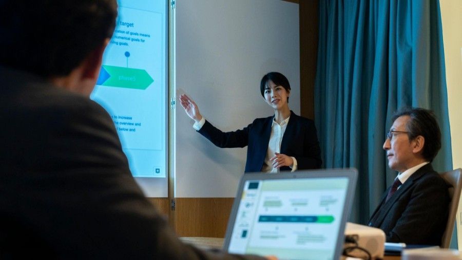 Business meeting presentation with a speaker pointing at a screen while colleagues listen in a conference room