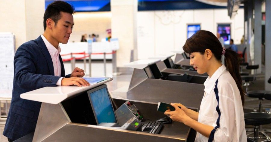 Two people using laptops at a service counter in a bright office or airport kiosk