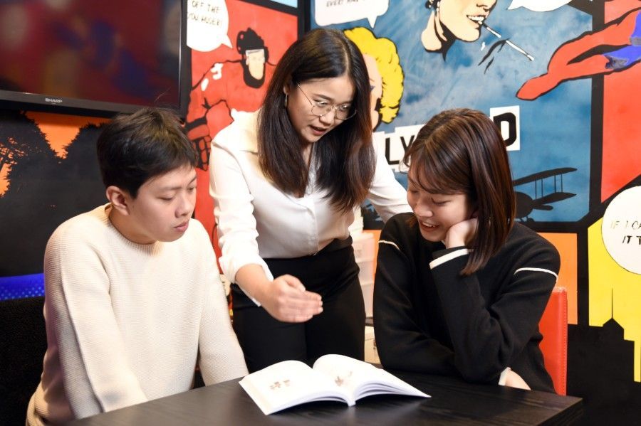 Three people gathered around a laptop at a table in a colorful indoor space