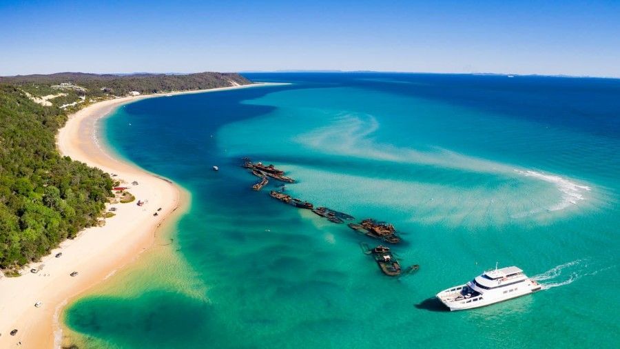 Aerial view of a turquoise bay with sandy beach, rocky outcrop, and a white boat near shore