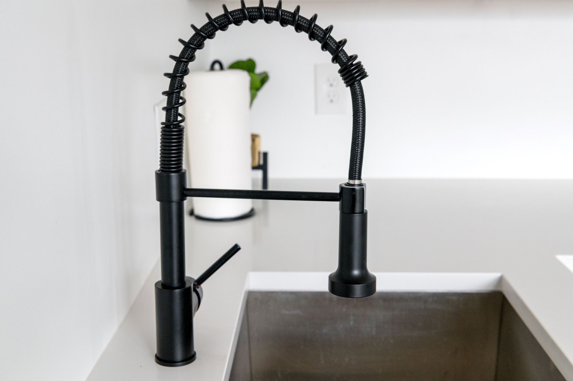 Black spring kitchen faucet beside a stainless steel sink on a white countertop