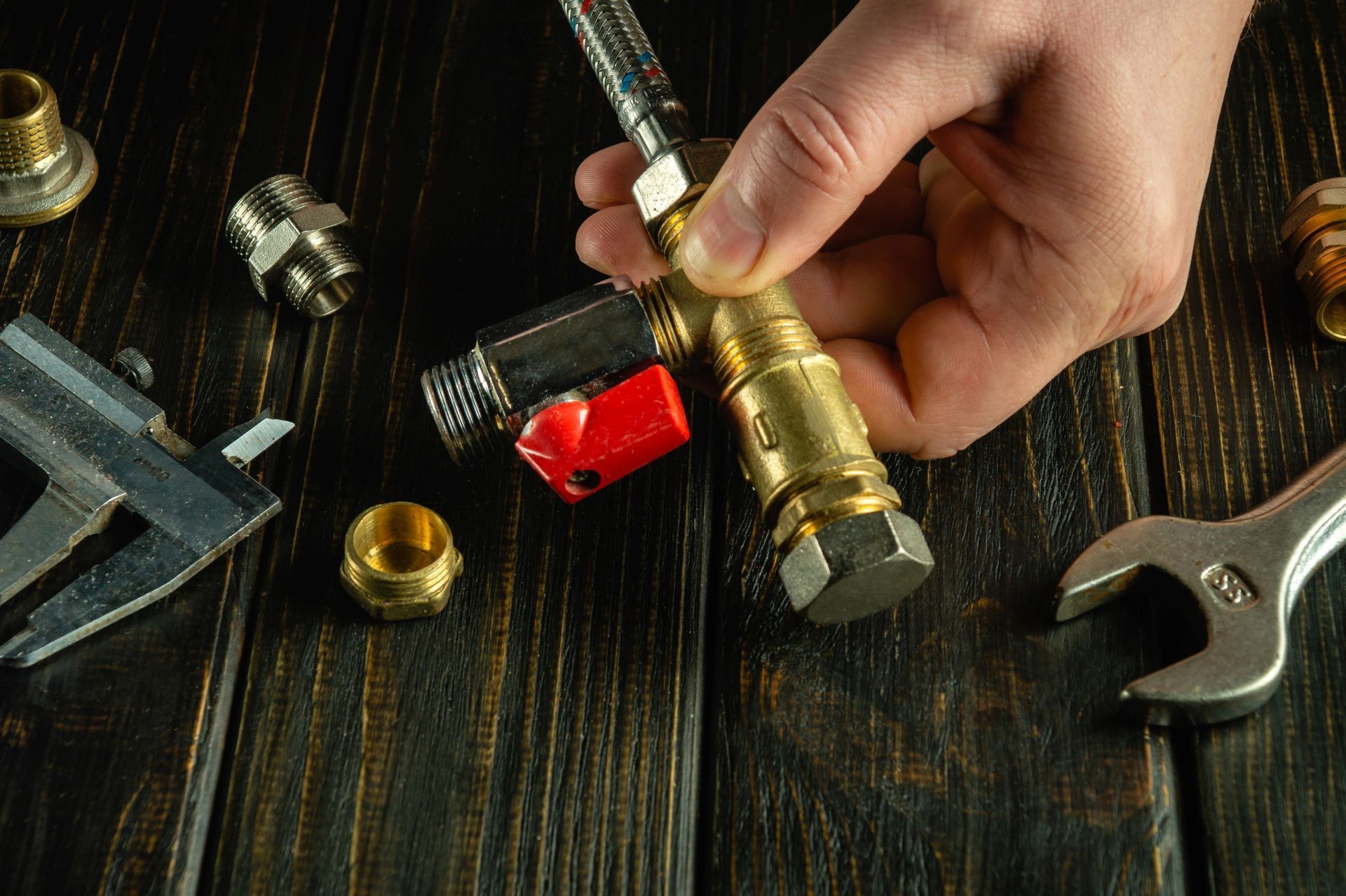 Hand holding a brass pipe fitting over assorted plumbing tools on a dark wooden workbench