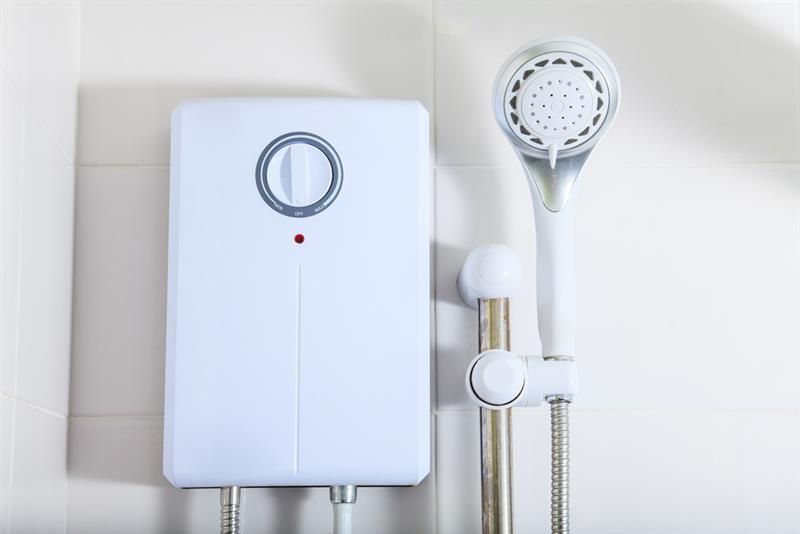 White shower water heater with handheld showerhead against tiled bathroom wall