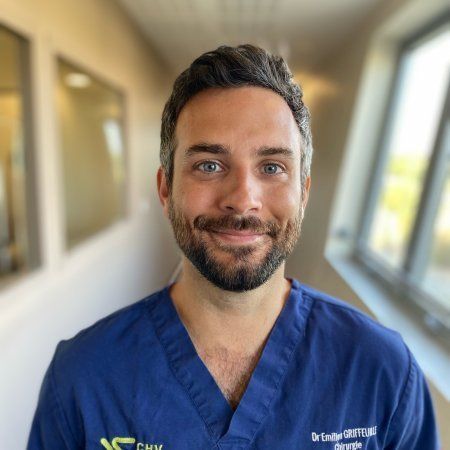 Un professionnel de santé souriant en blouse bleue se tient dans un couloir lumineux