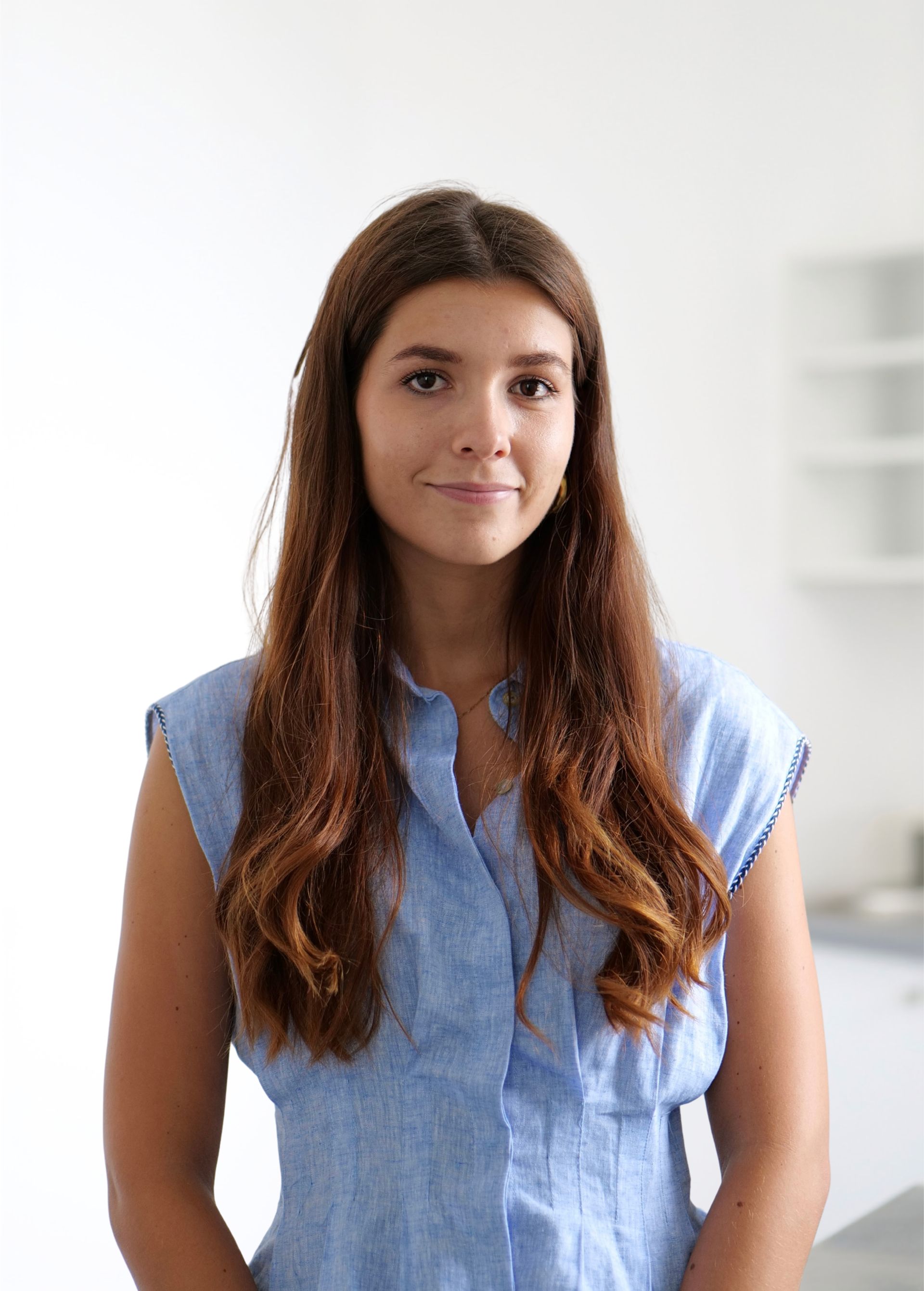 Femme aux longs cheveux bruns, vêtue d'un débardeur bleu clair, se détachant sur un fond blanc.