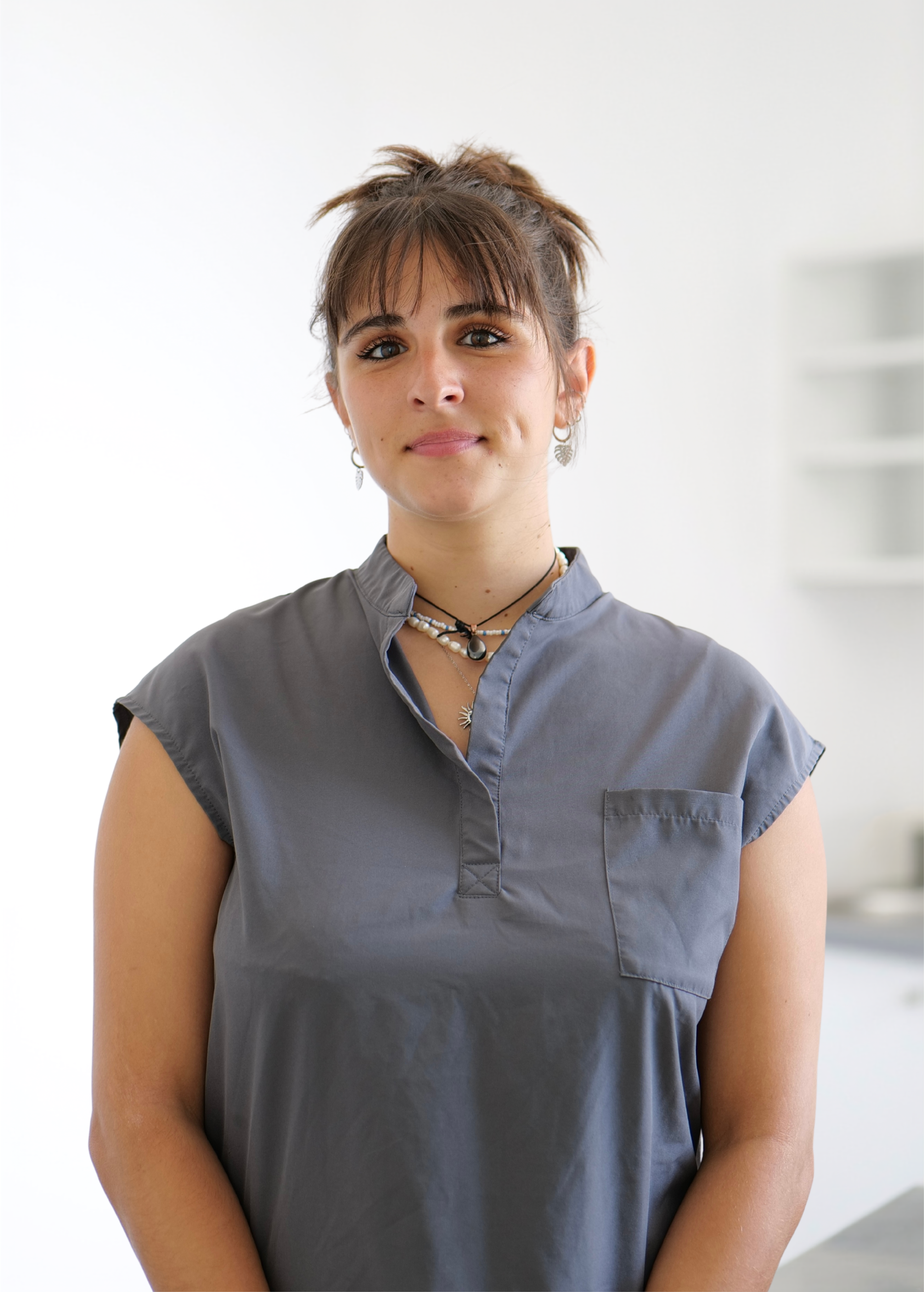 Personne vêtue d'un haut gris, debout à l'intérieur sur fond blanc.
