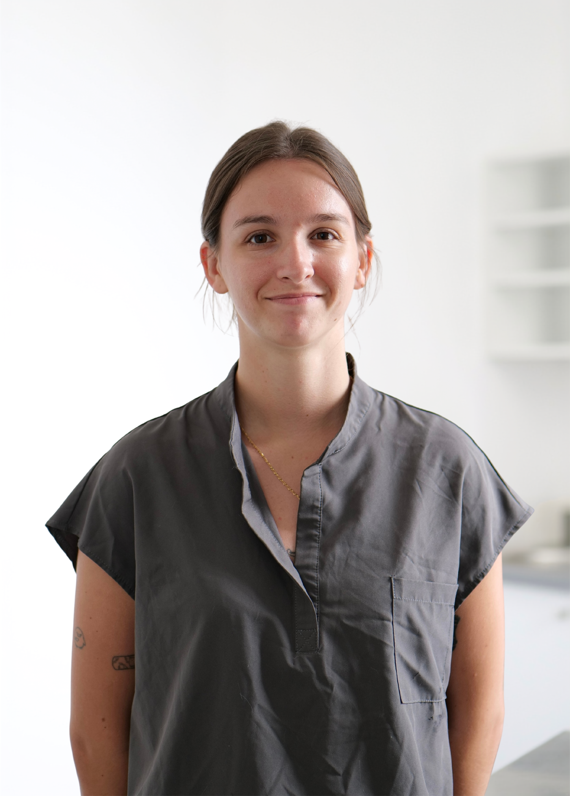 Personne se tenant sur un fond clair, portant une chemise gris foncé et arborant un léger sourire.