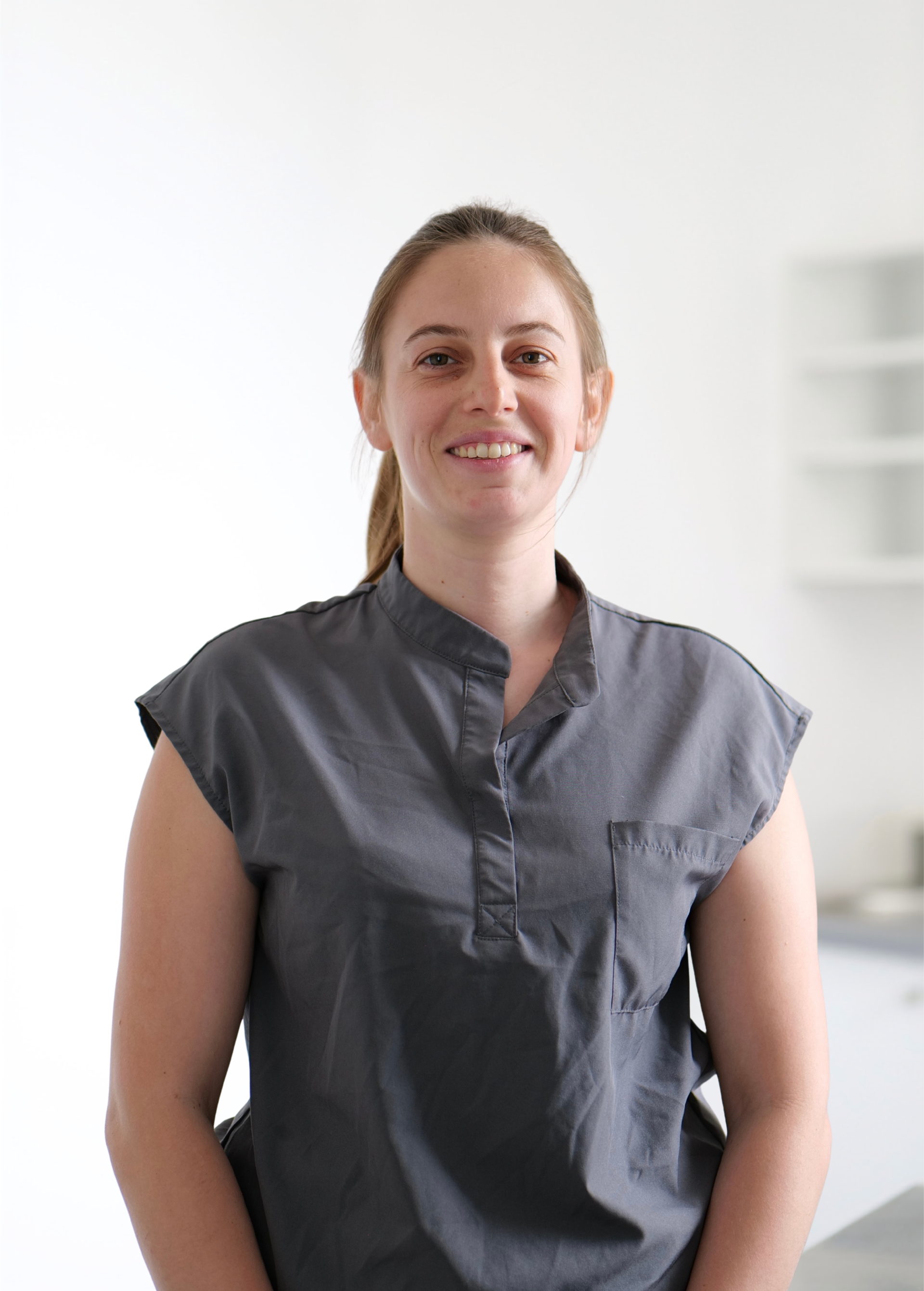 Personne souriante vêtue d'un débardeur gris, debout à l'intérieur sur fond blanc