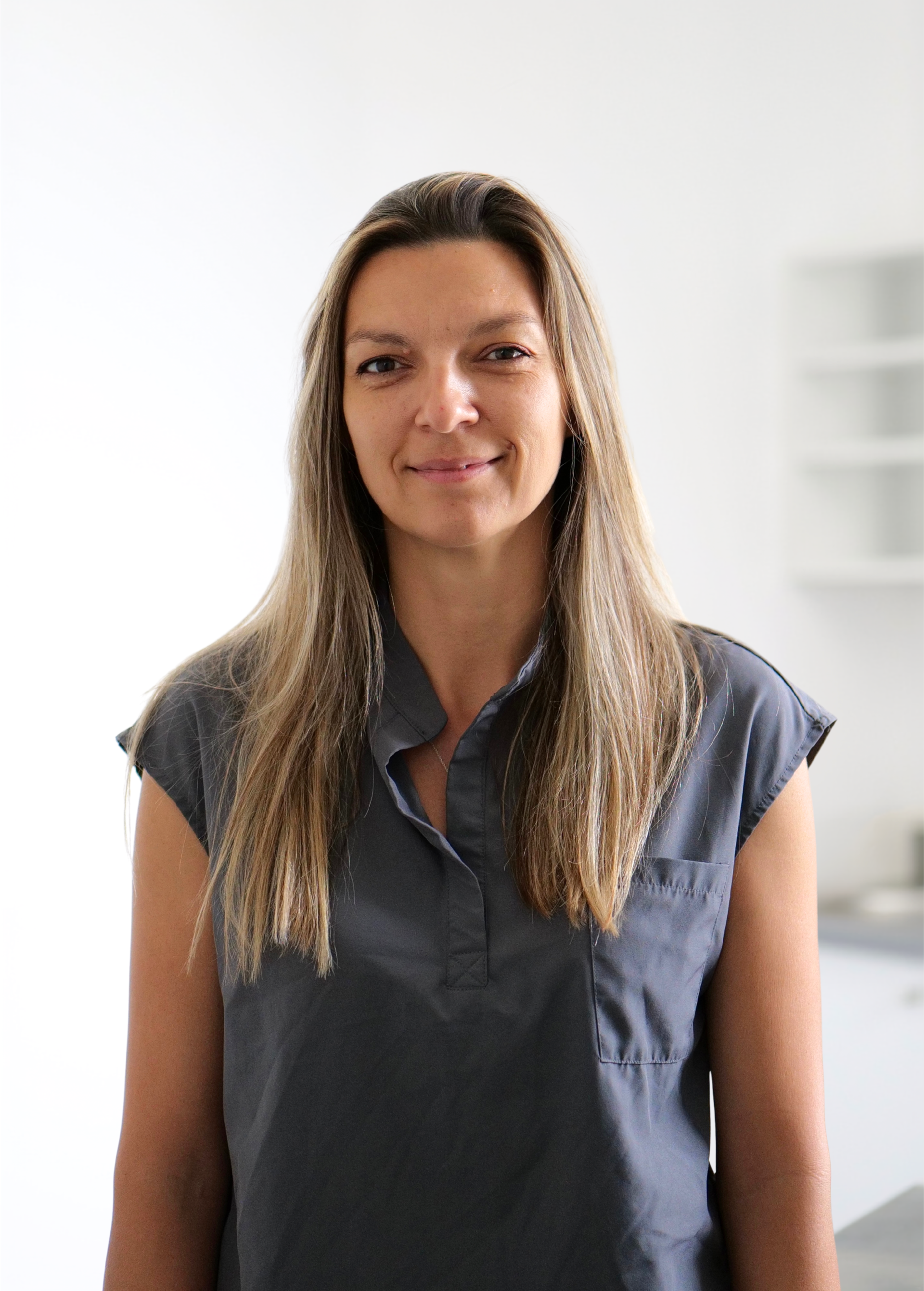 Portrait d'une femme souriante en chemise gris foncé sur fond intérieur lumineux