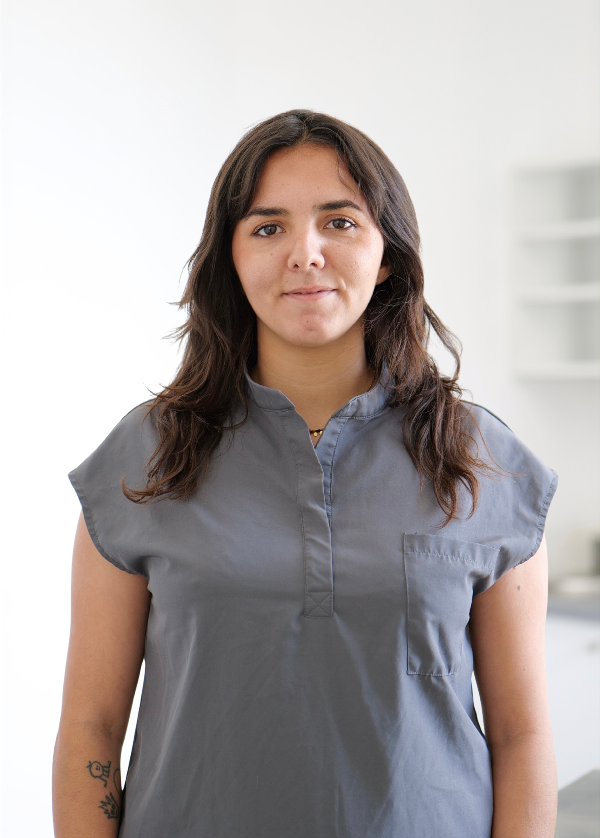 Personne debout à l'intérieur, contre un mur blanc, portant une chemise grise sans manches à boutons.