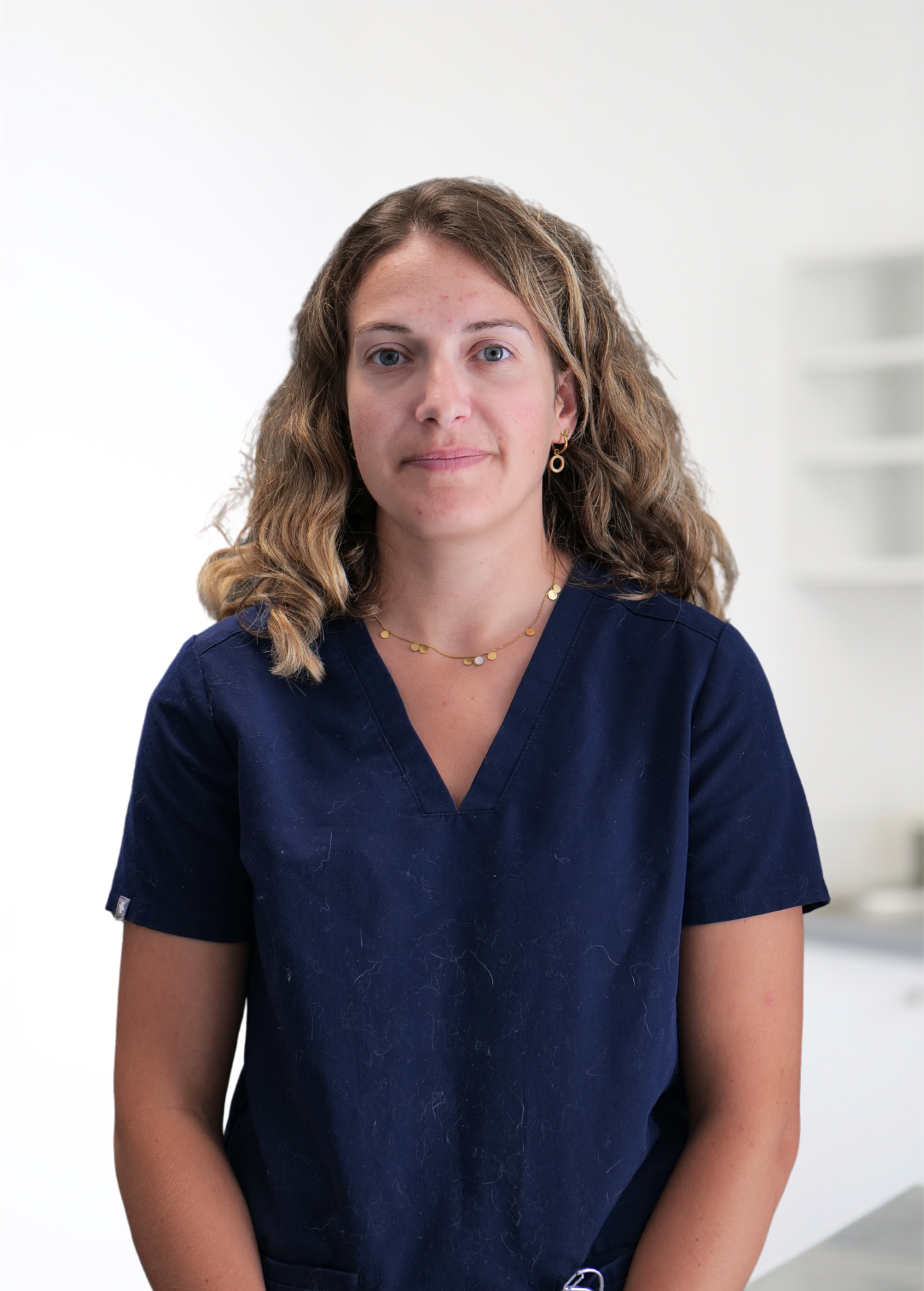 Femme debout à l'intérieur, vêtue d'un t-shirt bleu marine à col en V, regardant droit devant elle sur un fond blanc éclatant.