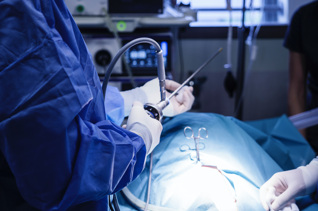 Des chirurgiens pratiquent une opération avec des instruments au-dessus d'un patient recouvert d'un drap chirurgical bleu.