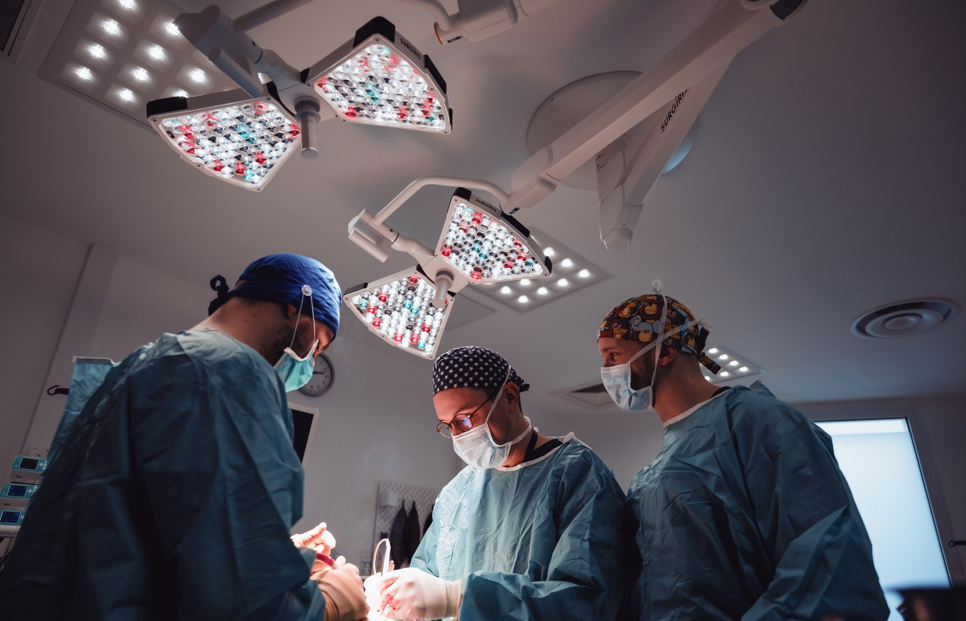 Des chirurgiens en blouse chirurgicale réalisent une opération sous la lumière vive du bloc opératoire.